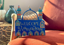 Load image into Gallery viewer, Royal blue ramadan and Eid welcome sign with gold and teal painted details. includes gems within design and gold accents. Shape of sign is a mosque with dome and two minarets.