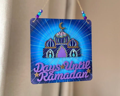 blue and turquoise plaque with mini mosque adorned with beads. Writing that says: Days until Ramadan, and it includes a few gold stars. Gold twine to hang, with beads on either side.