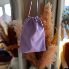 Load image into Gallery viewer, Purple drawstring bag hanging against a blurred indoor background with plants.