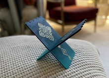 Load image into Gallery viewer, Blue metal book stand on a textured surface with a blurred indoor background