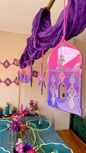 Load image into Gallery viewer, A decorative party setup with a purple draped fabric garland and hanging pink and purple arch-shaped ornaments, shown above a decorated table in an indoor room.