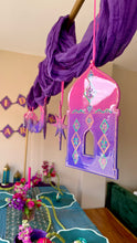 Load image into Gallery viewer, A purple and pink hanging decorative lantern ornament with geometric patterns, suspended from a draped purple fabric garland in an indoor room setting.