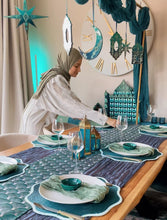 Load image into Gallery viewer, muslim Woman hijabi setting a ramadan table with decorative items  and ornaments in a room with a star and moon design and ramadan calendar